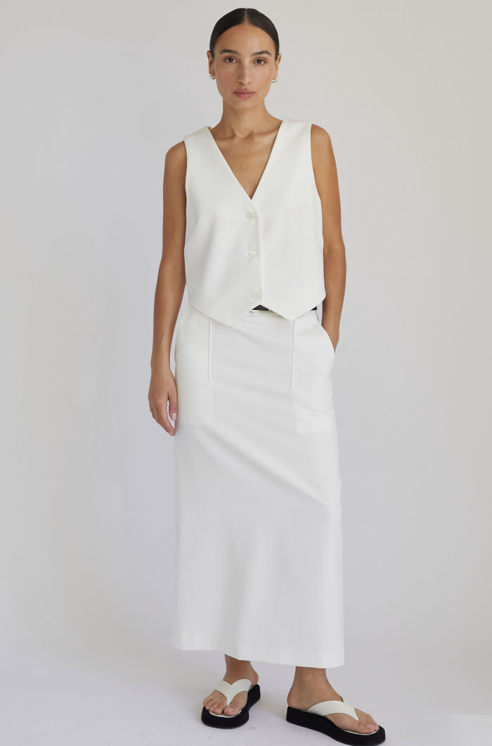 Woman wearing a white sleeveless top and skirt set on a plain background