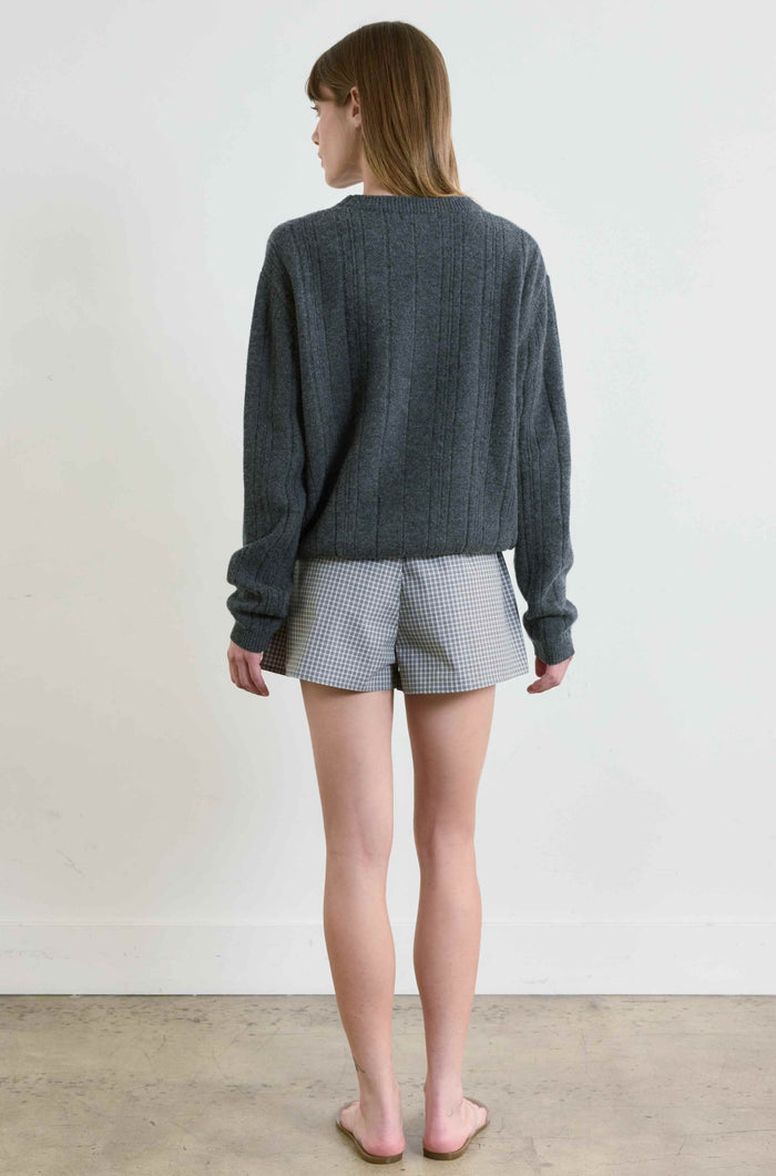 Person wearing a gray sweater and checkered shorts against a plain background