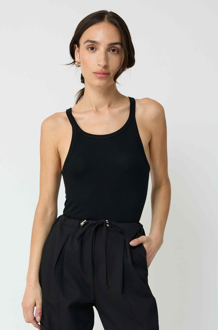 Woman wearing a black tank top and black pants against a white background