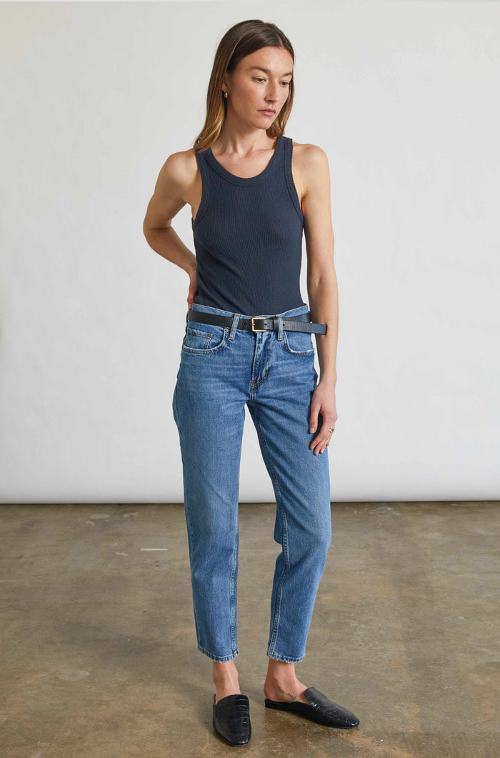Woman wearing a navy tank top and blue jeans standing against a plain background
