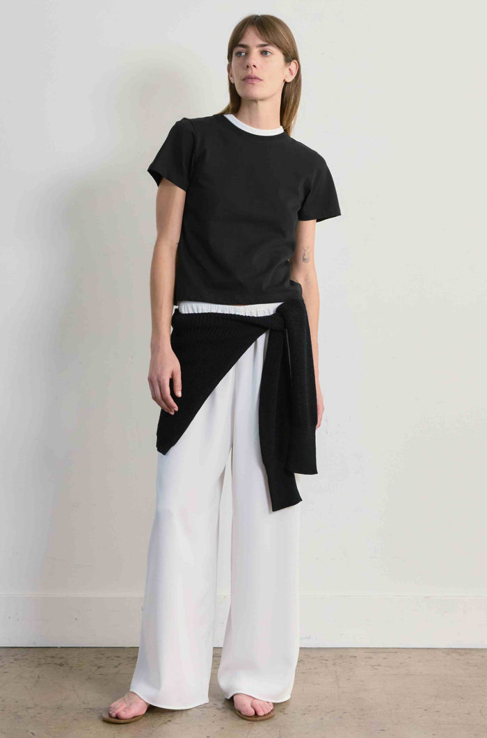 Woman wearing a black top and white pants against a plain background