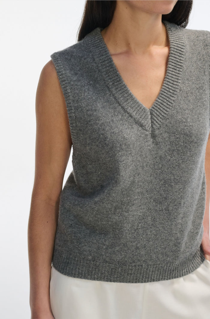 Gray knitted vest worn by a person on a white background